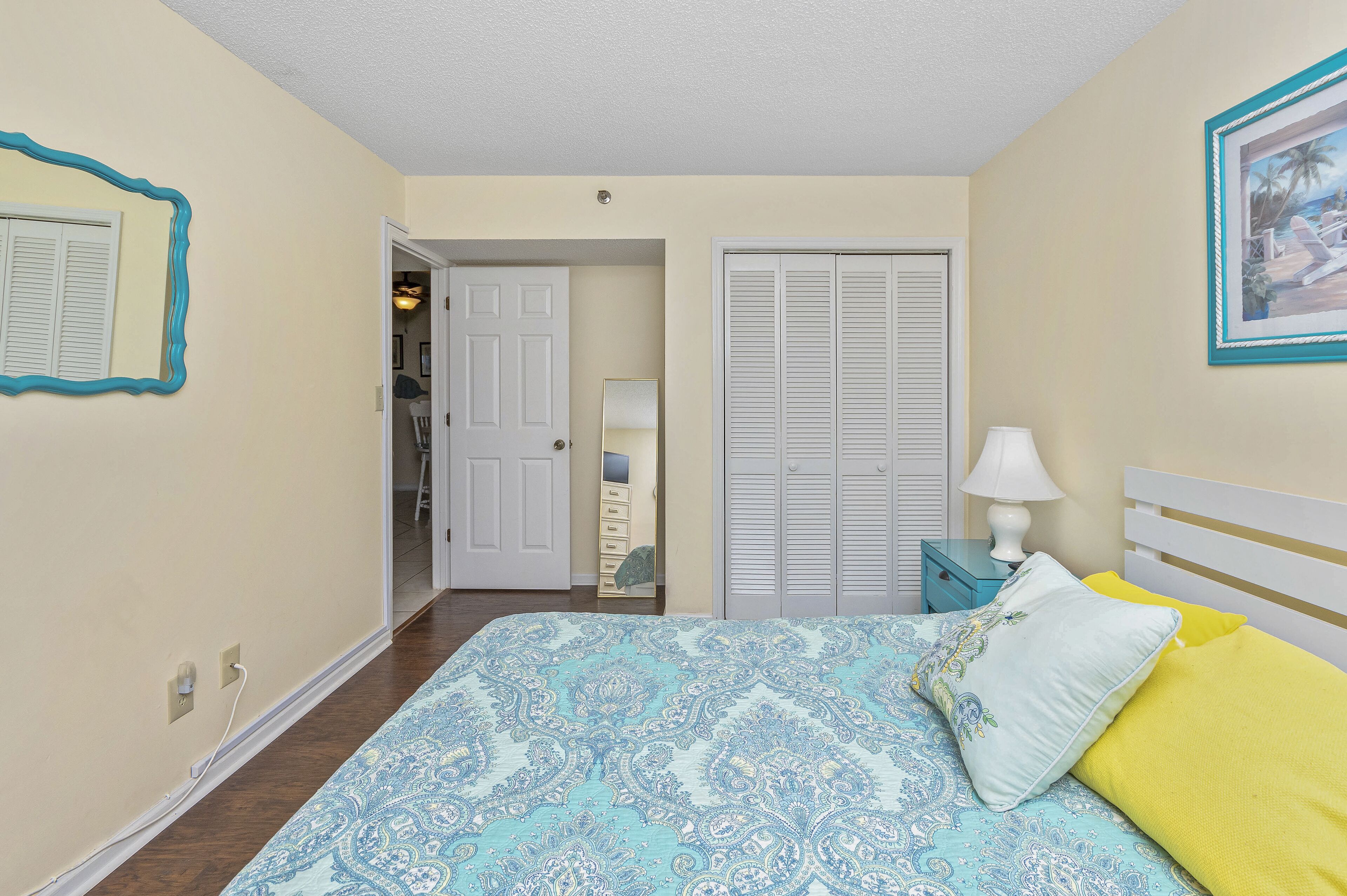 A bedroom with a bed, a nightstand, a lamp, a door, and a closet.