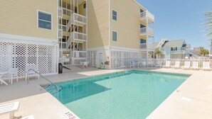 A pool area with a clear blue pool, white lounge chairs, and a building with balconies. - Immaculate two bedroom, two bath oceanview condo located in the heart of North Myrtle Beach!! (North Myrtle Beach)