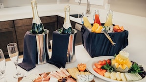 Velorganiseret anretning med forskellig ost, kød og frugt på en træplanke, ledsaget af champagne og juice i metalspande.