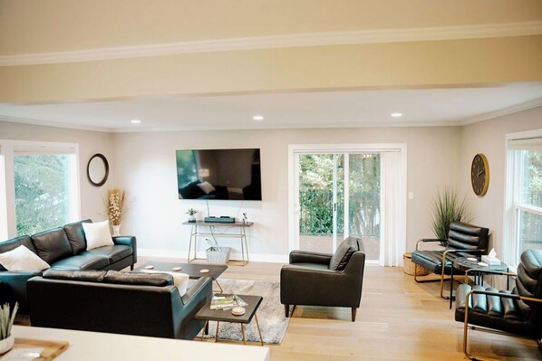 A modern living room with a flat-screen TV, leather sofas, and a large window.