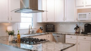 Una cucina moderna con mobili bianchi, una grande isola con piano cottura a gas, cappa aspirante in acciaio inossidabile e forno a microonde.