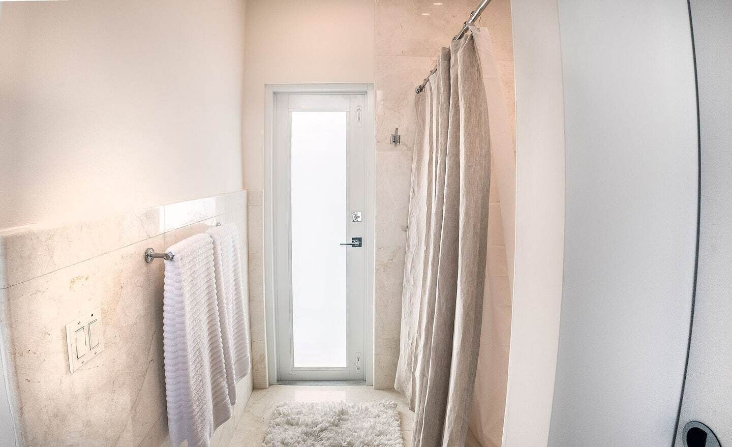 A narrow bathroom with a white door, a towel rack, and a shower curtain.