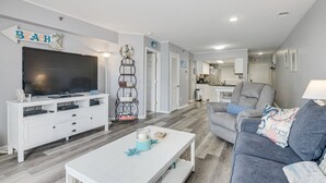 Ett modernt vardagsrum med en platt-TV, en vit TV-bänk, en grå soffa och ett soffbord.