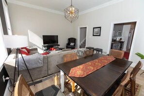 Een moderne woonkamer met een bank, een eettafel, een televisie en een keuken op de achtergrond.