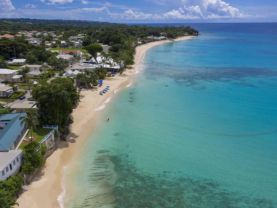 Eine Luftaufnahme einer Küstenregion mit einem Sandstrand, klarem türkisblauem Wasser und Wohngebäuden entlang der Uferlinie.
