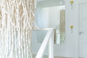 A modern interior with a white staircase, a beaded curtain, and a wall-mounted light fixture.