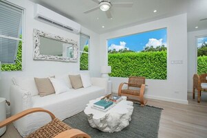 A modern living room with a white sofa, a round coffee table, and a large window with a view of greenery.