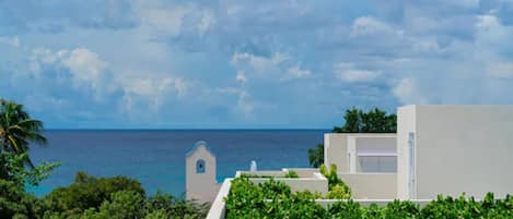 A coastal view with a white building, greenery, and a clear sky.