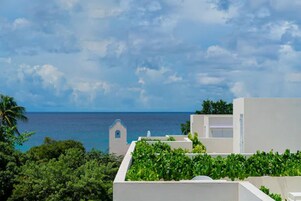 Vista costera con un edificio blanco, vegetación y cielo despejado.