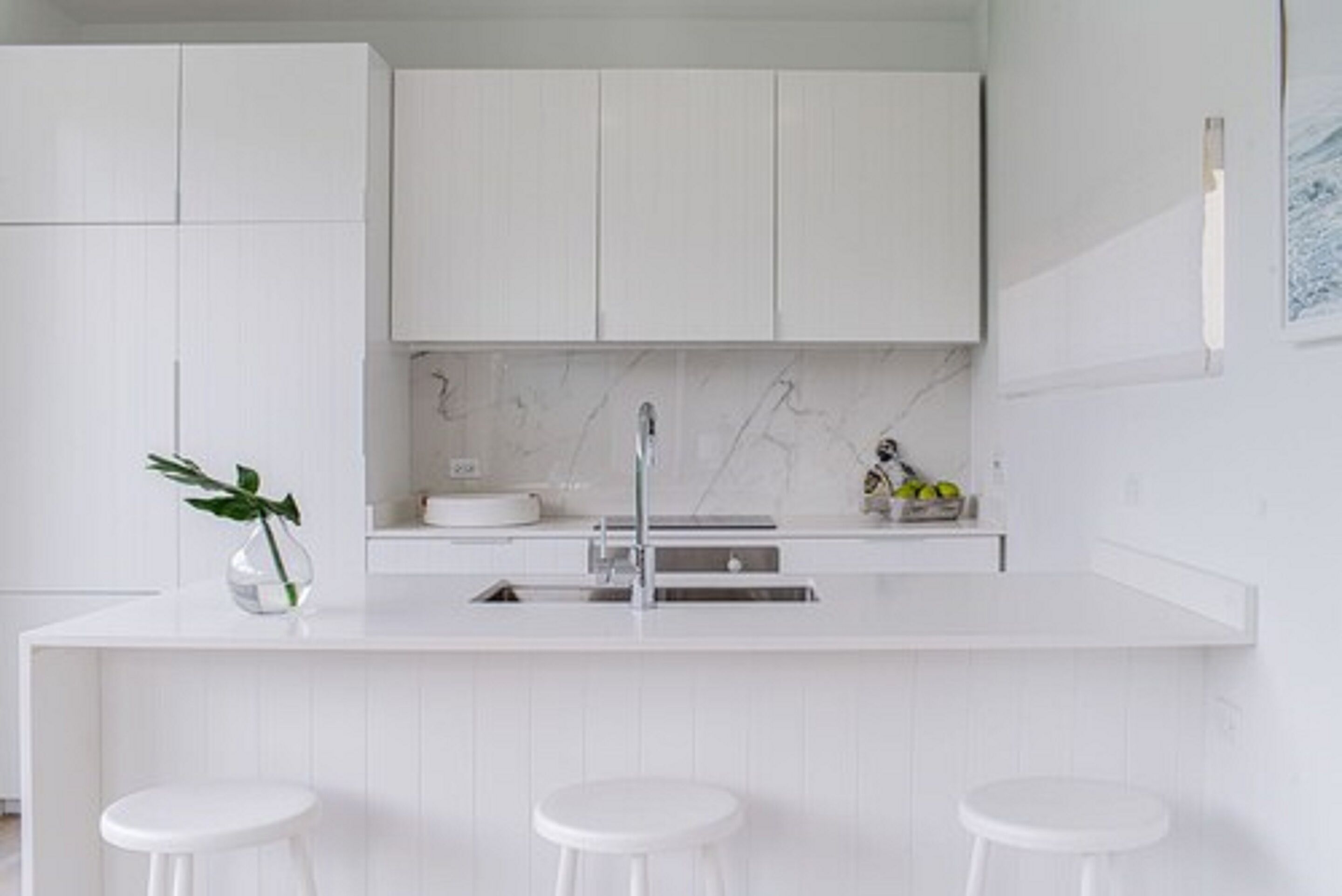 A modern kitchen with white cabinetry, a marble backsplash, and a central island with stools.