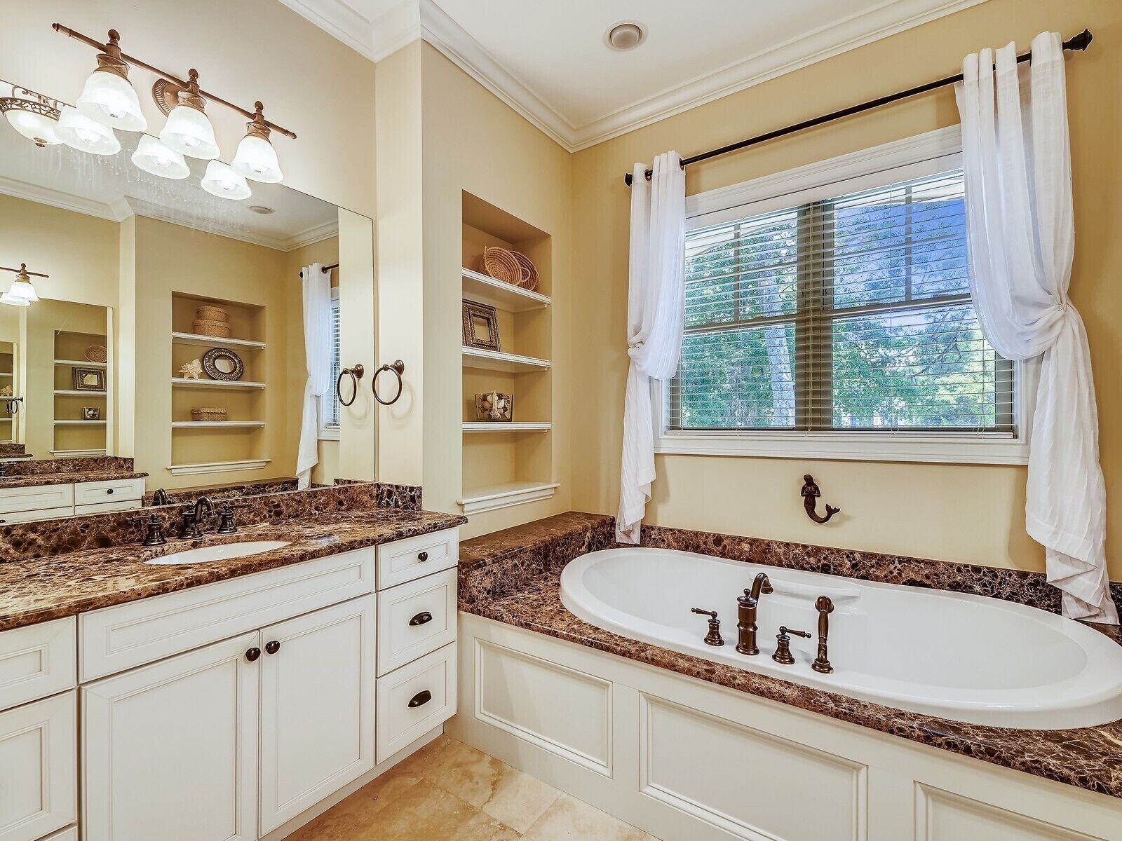 A bathroom with a large freestanding bathtub, a vanity with a marble countertop, and a window with curtains.