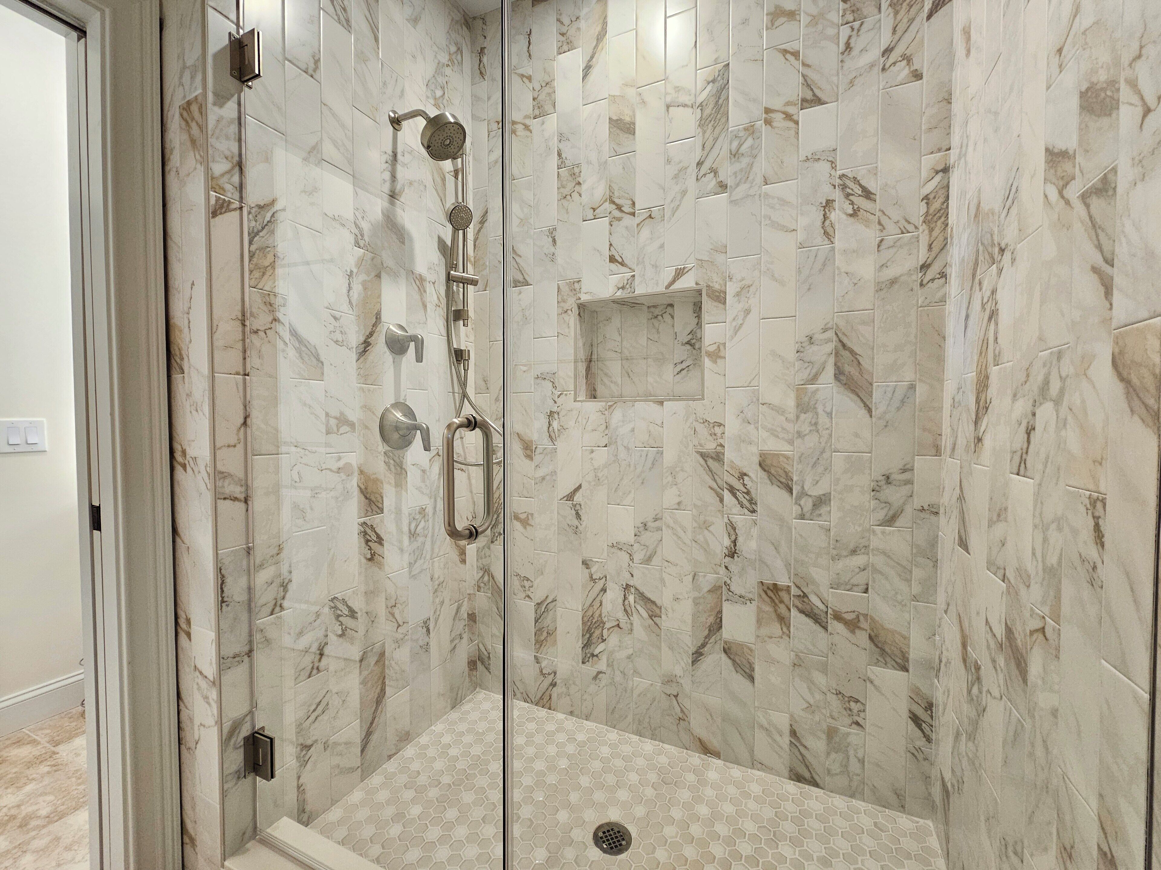 Une douche à l’italienne avec une porte en verre, des carreaux de marbre et un sol recouvert de carreaux hexagonaux.