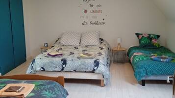 A bedroom with a large bed, two smaller beds, a wall clock, a bedside table with a lamp, and a wall with a motivational quote.