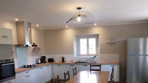 A modern kitchen with a wooden dining table, white cabinets, a built-in oven, and a stainless steel refrigerator. - Grande Longère (ploezal)