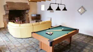 A pool table in a room with a yellow sofa, a fireplace, and a television. - Grande Longère (ploezal)