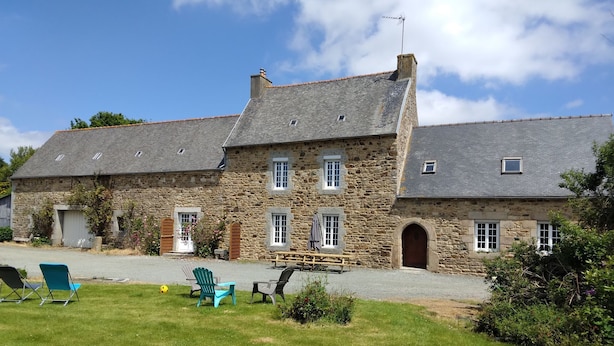 A stone building with a sloped roof, multiple windows, and a small porch area. - Grande Longère (ploezal)