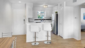 Una cocina moderna con armarios blancos, electrodomésticos de acero inoxidable y una isla central con taburetes de bar.