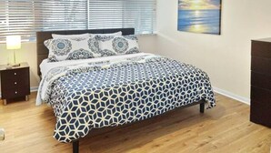 Un dormitorio con una cama, una mesita de noche, un aparador y un cuadro en la pared.
