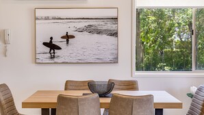 Un comedor con una mesa de madera, sillas de cuero y una fotografía enmarcada de surfistas en la playa.