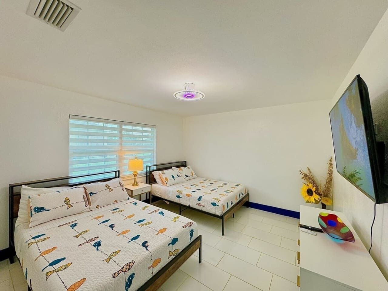Ein Zimmer mit zwei Betten, einem Fernseher und einem Fenster mit Jalousien.