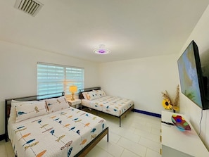 Een kamer met twee bedden, een televisie en een raam met zonwering.