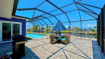Eine Terrasse im Freien mit Grill, Sitzgelegenheit und Blick auf einen Swimmingpool.