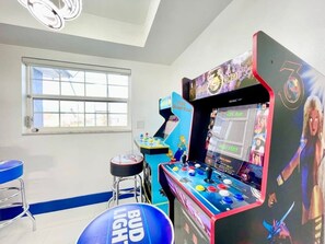 A room with arcade machines, a window, and a blue bar stool. - Gulf access home with heated pool & dock (Cape Coral)