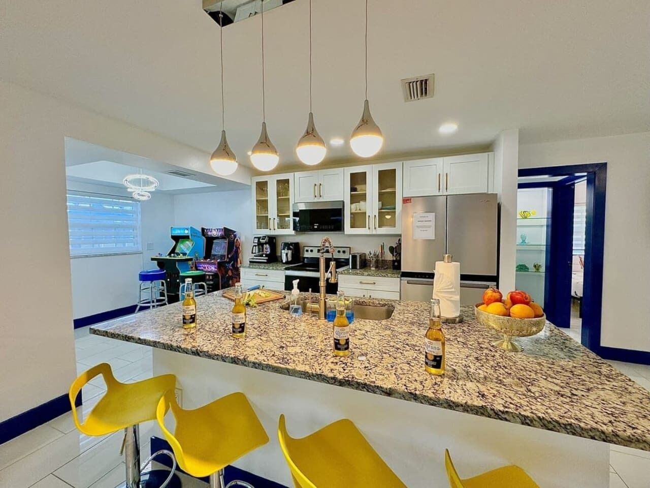 Una cocina moderna con encimeras de granito, armarios blancos y una isla central con taburetes de bar.