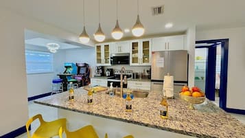 Una cocina moderna con encimeras de granito, armarios blancos y una isla central con taburetes de bar.