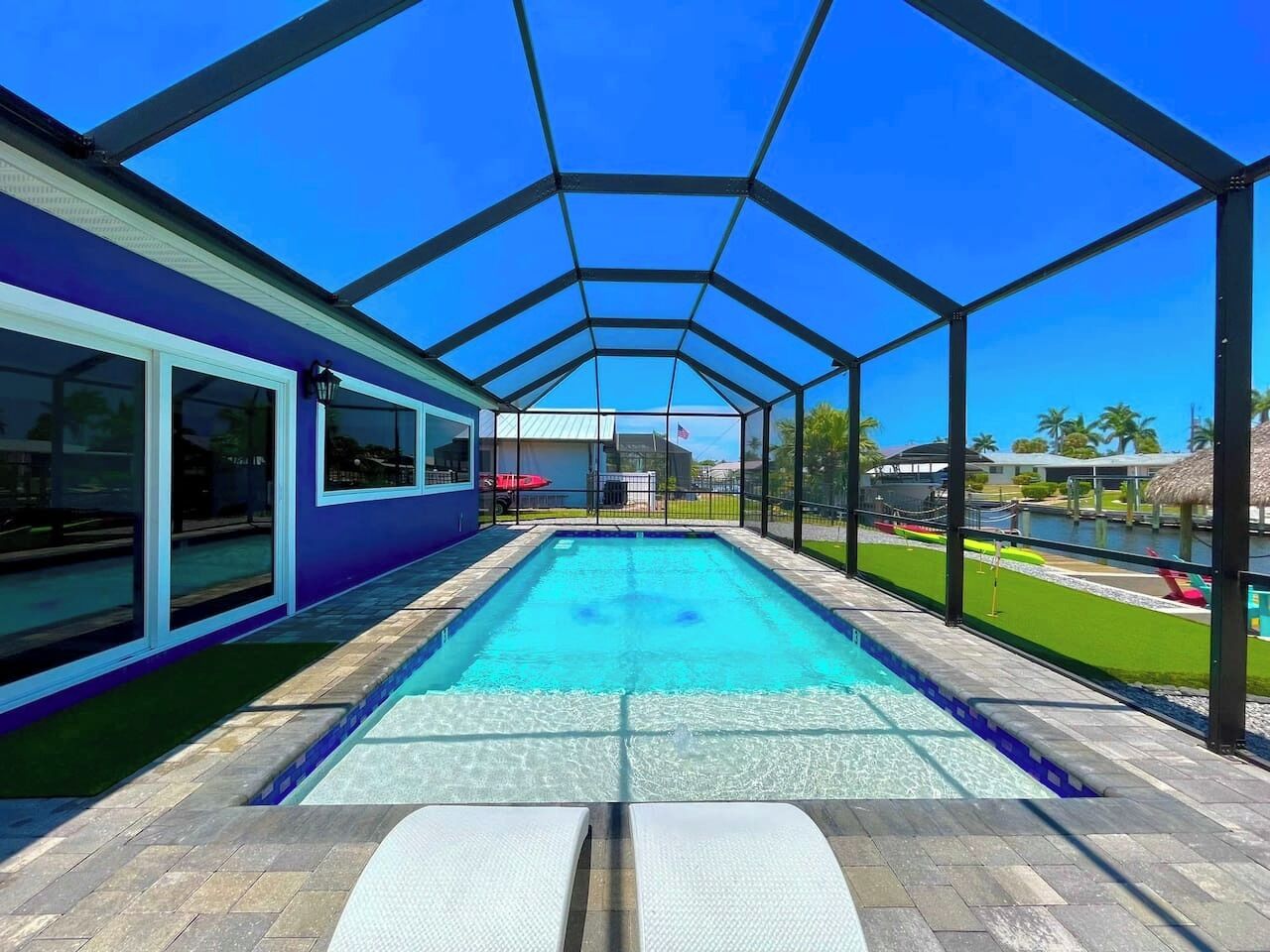 A swimming pool with a glass enclosure, surrounded by a patio area with a view of a body of water and palm trees.