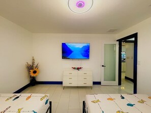 A room with a flat-screen TV mounted on the wall, a white dresser, and a bed with a patterned bedspread. - Gulf access home with heated pool & dock (Cape Coral)
