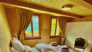 Quarto de cabana de madeira com uma cama, duas janelas e uma cadeira.