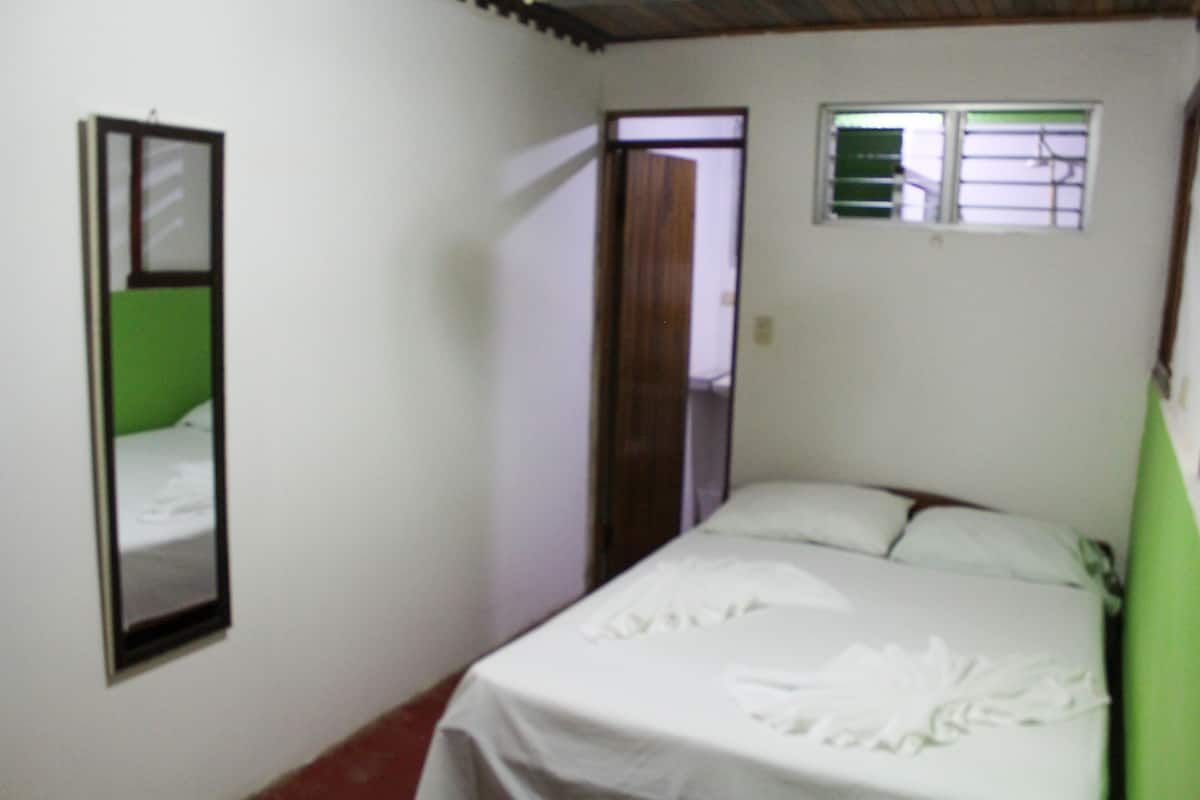 A small, simple room with a bed, a mirror, and a window.