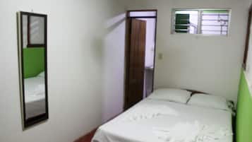 A small, simple room with a bed, a mirror, and a window.