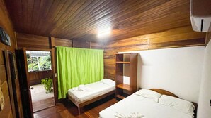 Una habitación de madera con dos camas, una cortina verde y una mesita con un control remoto.