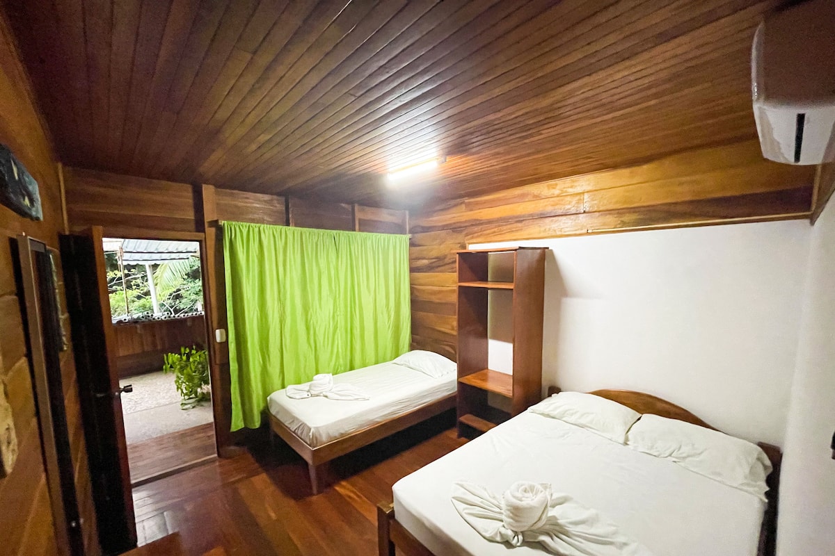A wooden room with two beds, a green curtain, and a small table with a remote control.