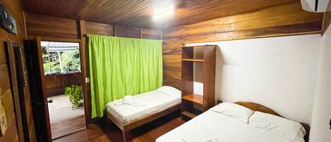 A wooden room with two beds, a green curtain, and a small table with a remote control.