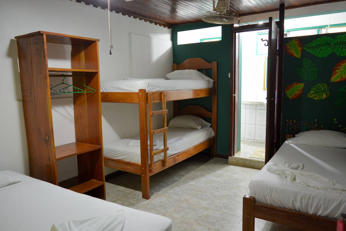 A dormitory room with bunk beds, a wooden shelf unit, and a single bed.