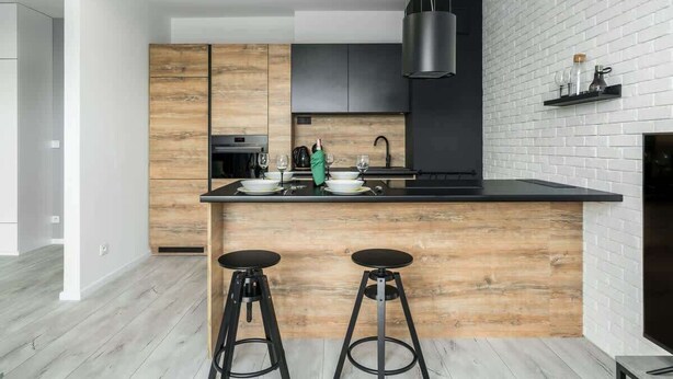 Una cocina moderna con una isla de madera, taburetes negros y un salpicadero de ladrillo blanco.