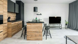 Una cocina moderna con una isla central, taburetes de bar, un televisor de pantalla plana y un diseño minimalista con paredes de ladrillo blanco y detalles de madera.