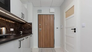 A modern kitchen with white cabinets, a dark countertop, and a wooden door. - Modern Studio | Parking | Air Conditioning | Close to Expo XXI (Warszawa)