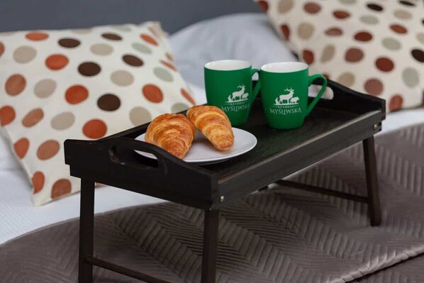 A bed with polka dot pillows, a tray with croissants and green mugs, and a bedspread with a herringbone pattern.