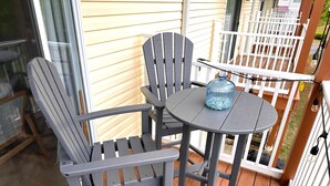 Une terrasse avec deux fauteuils Adirondack et une petite table ronde, un vase en verre bleu et une clôture blanche à lattes.