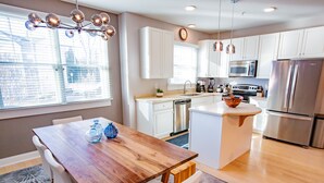 Une cuisine moderne avec des meubles blancs, des appareils en acier inoxydable et une table à manger en bois.