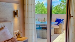 Ein Schlafzimmer mit einem großen Bett, einem Nachttisch und Blick auf eine Terrasse mit Tisch und Stühlen.