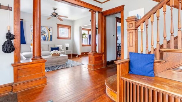A spacious living room with hardwood floors, a wooden staircase, and a large window.