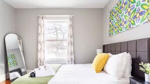 A neatly arranged bedroom with a bed, a bedside table, a mirror, and a window with curtains.