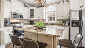 A kitchen with white cabinets, stainless steel appliances, a granite countertop, and a central island with chairs.
