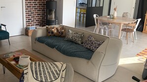 A cozy living room with a sofa, a coffee table, and a foosball table. There is a brick wall, a fireplace, and a dining area in the background. - 150m² house with views of the countryside and the Golfe du Morbihan (Baden)