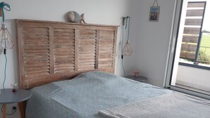 A bedroom with a wooden headboard, a patterned bedspread, a bedside table, and a window with a view of greenery. - 150m² house with views of the countryside and the Golfe du Morbihan (Baden)
